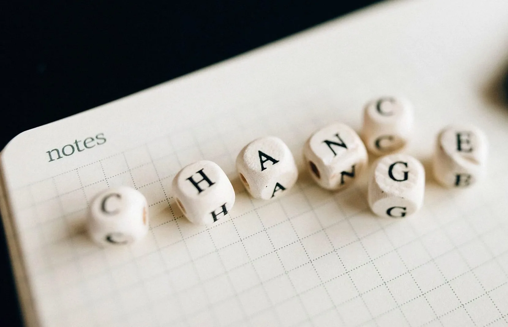 格子状のメモ帳の上に「change」と並んだレタータイルのクローズアップ。変革を象徴する。